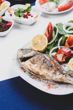 Kızarmış deniz çerezi (cupra) beyaz tabakta soğan, bahçe roketi ve limon dilimli balık.