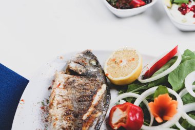 Kızarmış deniz çerezi (cupra) beyaz tabakta soğan, bahçe roketi ve limon dilimli balık.