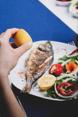 Kızarmış deniz çerezi (cupra) beyaz tabakta soğan, bahçe roketi ve limon dilimli balık.