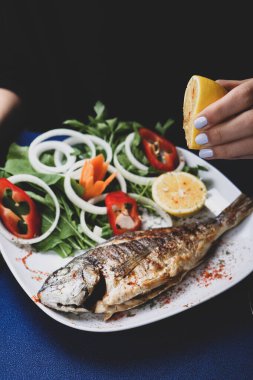Kızarmış deniz çerezi (cupra) beyaz tabakta soğan, bahçe roketi ve limon dilimli balık.