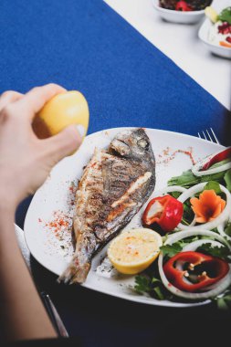 Kızarmış deniz çerezi (cupra) beyaz tabakta soğan, bahçe roketi ve limon dilimli balık.