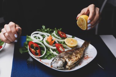 Kızarmış deniz çerezi (cupra) beyaz tabakta soğan, bahçe roketi ve limon dilimli balık.