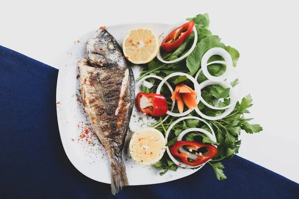 Kızarmış deniz çerezi (cupra) beyaz tabakta soğan, bahçe roketi ve limon dilimli balık.