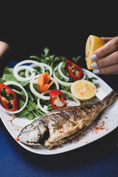 Kızarmış deniz çerezi (cupra) beyaz tabakta soğan, bahçe roketi ve limon dilimli balık.