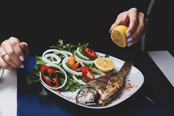 Kızarmış deniz çerezi (cupra) beyaz tabakta soğan, bahçe roketi ve limon dilimli balık.