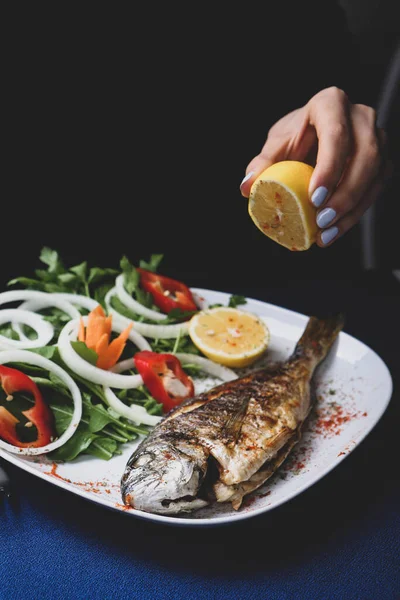 Kızarmış deniz çerezi (cupra) beyaz tabakta soğan, bahçe roketi ve limon dilimli balık.