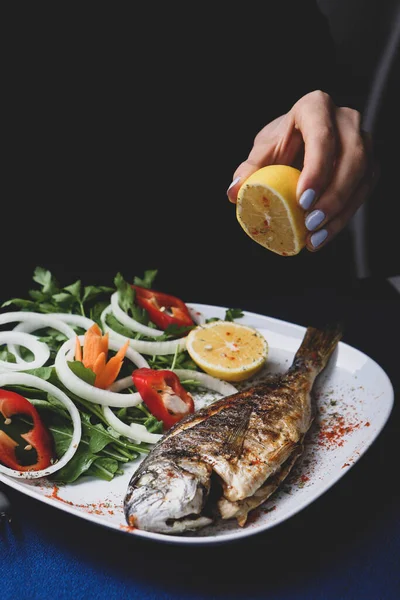Kızarmış deniz çerezi (cupra) beyaz tabakta soğan, bahçe roketi ve limon dilimli balık.