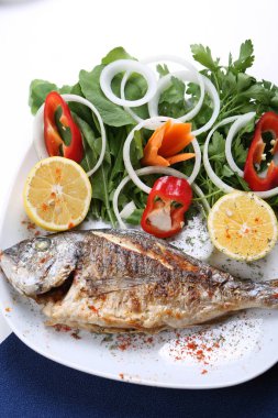 Kızarmış deniz çerezi (cupra) beyaz tabakta soğan, bahçe roketi ve limon dilimli balık.