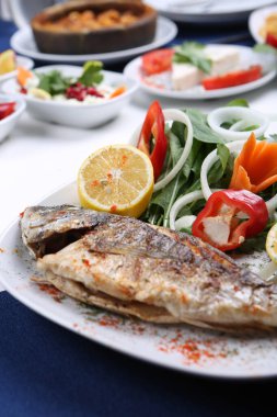 Kızarmış deniz çerezi (cupra) beyaz tabakta soğan, bahçe roketi ve limon dilimli balık.