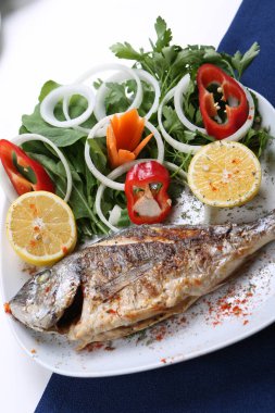 Kızarmış deniz çerezi (cupra) beyaz tabakta soğan, bahçe roketi ve limon dilimli balık.