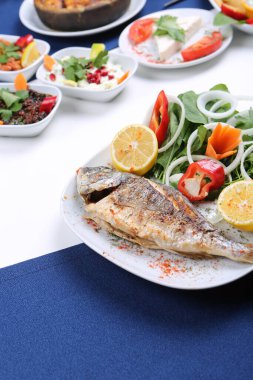 Kızarmış deniz çerezi (cupra) beyaz tabakta soğan, bahçe roketi ve limon dilimli balık.