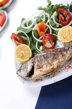 Kızarmış deniz çerezi (cupra) beyaz tabakta soğan, bahçe roketi ve limon dilimli balık.