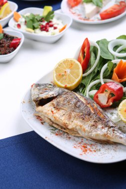 Kızarmış deniz çerezi (cupra) beyaz tabakta soğan, bahçe roketi ve limon dilimli balık.