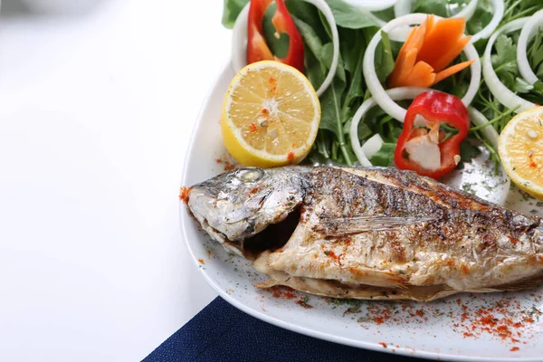 Kızarmış deniz çerezi (cupra) beyaz tabakta soğan, bahçe roketi ve limon dilimli balık.