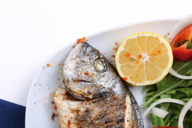 Kızarmış deniz çerezi (cupra) beyaz tabakta soğan, bahçe roketi ve limon dilimli balık.