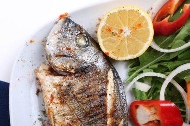 Kızarmış deniz çerezi (cupra) beyaz tabakta soğan, bahçe roketi ve limon dilimli balık.