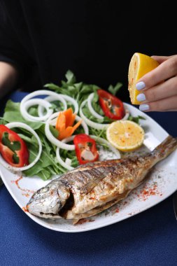 Kızarmış deniz çerezi (cupra) beyaz tabakta soğan, bahçe roketi ve limon dilimli balık.