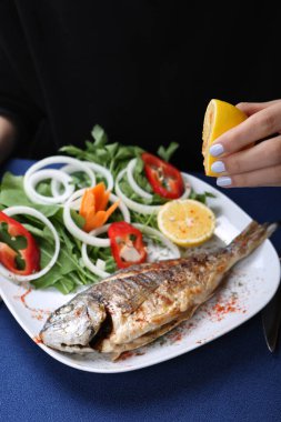 Kızarmış deniz çerezi (cupra) beyaz tabakta soğan, bahçe roketi ve limon dilimli balık.