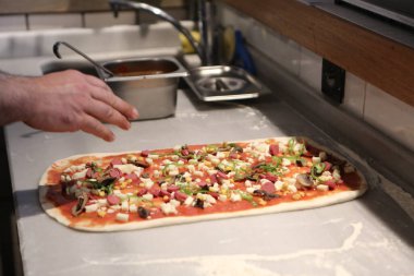 Pizza şefi ticari bir mutfakta sosu tabana koydu.