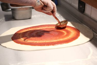 Pizza şefi ticari bir mutfakta sosu tabana koydu.