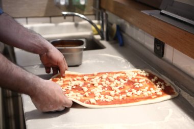 Pizza şefi ticari bir mutfakta sosu tabana koydu.