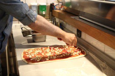 Pizza şefi ticari bir mutfakta sosu tabana koydu.