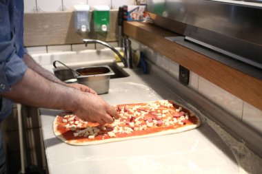 Pizza şefi ticari bir mutfakta sosu tabana koydu.