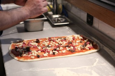 Pizza şefi ticari bir mutfakta sosu tabana koydu.