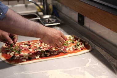 Pizza şefi ticari bir mutfakta sosu tabana koydu.