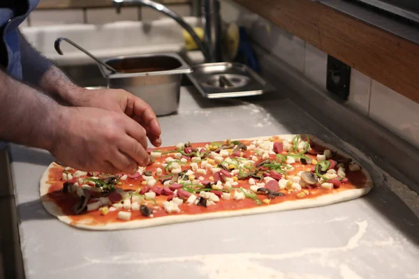 Pizza şefi ticari bir mutfakta sosu tabana koydu.