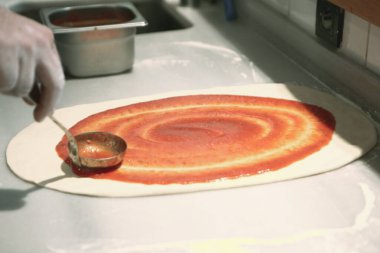 Pizza şefi ticari bir mutfakta sosu tabana koydu.