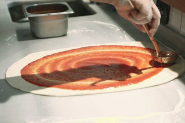 Pizza şefi ticari bir mutfakta sosu tabana koydu.