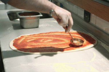 Pizza şefi ticari bir mutfakta sosu tabana koydu.