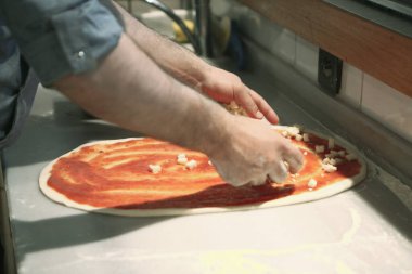 Pizza şefi ticari bir mutfakta sosu tabana koydu.