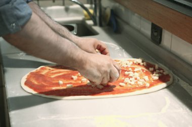 Pizza şefi ticari bir mutfakta sosu tabana koydu.