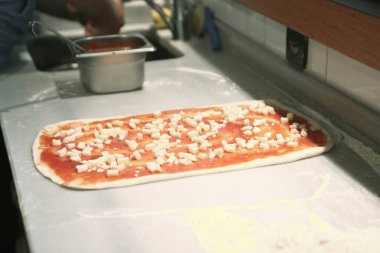 Pizza şefi ticari bir mutfakta sosu tabana koydu.