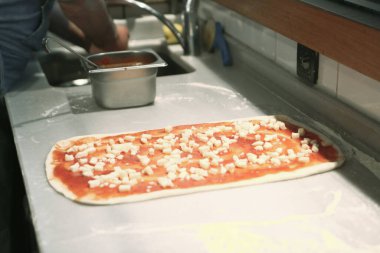 Pizza şefi ticari bir mutfakta sosu tabana koydu.