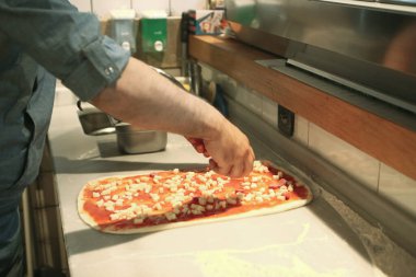 Pizza şefi ticari bir mutfakta sosu tabana koydu.