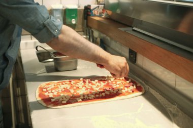 Pizza şefi ticari bir mutfakta sosu tabana koydu.