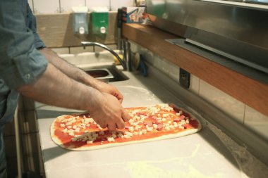 Pizza şefi ticari bir mutfakta sosu tabana koydu.
