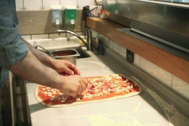 Pizza şefi ticari bir mutfakta sosu tabana koydu.