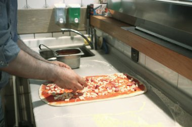 Pizza şefi ticari bir mutfakta sosu tabana koydu.