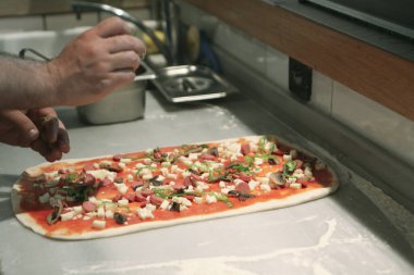 Pizza şefi ticari bir mutfakta sosu tabana koydu.