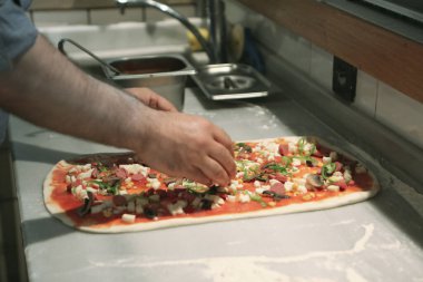 Pizza şefi ticari bir mutfakta sosu tabana koydu.