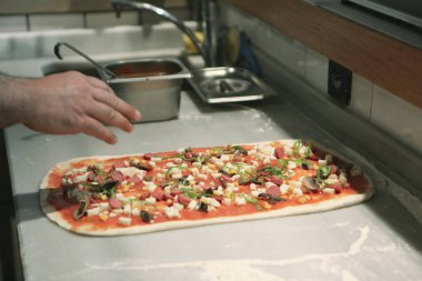 Pizza şefi ticari bir mutfakta sosu tabana koydu.