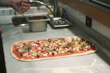 Pizza şefi ticari bir mutfakta sosu tabana koydu.