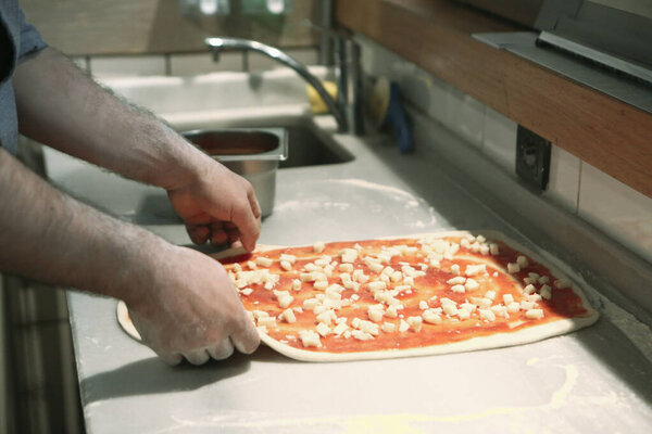 Pizza chef put sauce on base in a commercial kitchen