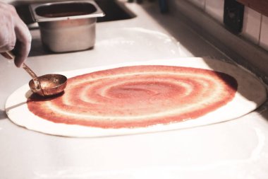 Pizza şefi ticari bir mutfakta sosu tabana koydu.