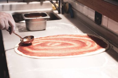 Pizza şefi ticari bir mutfakta sosu tabana koydu.