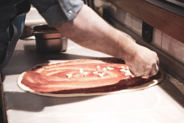 Pizza şefi ticari bir mutfakta sosu tabana koydu.